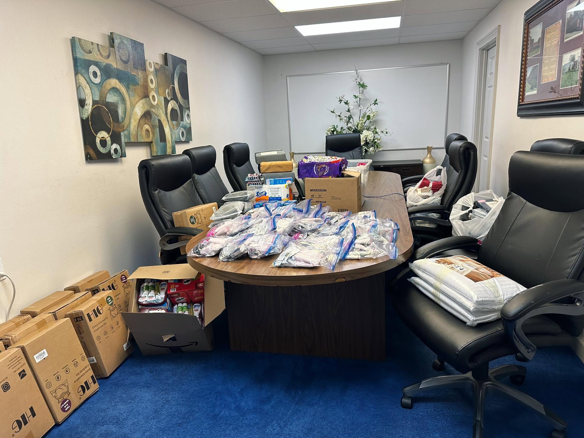A conference table piled with donated hygiene kits, bedding, and supplies