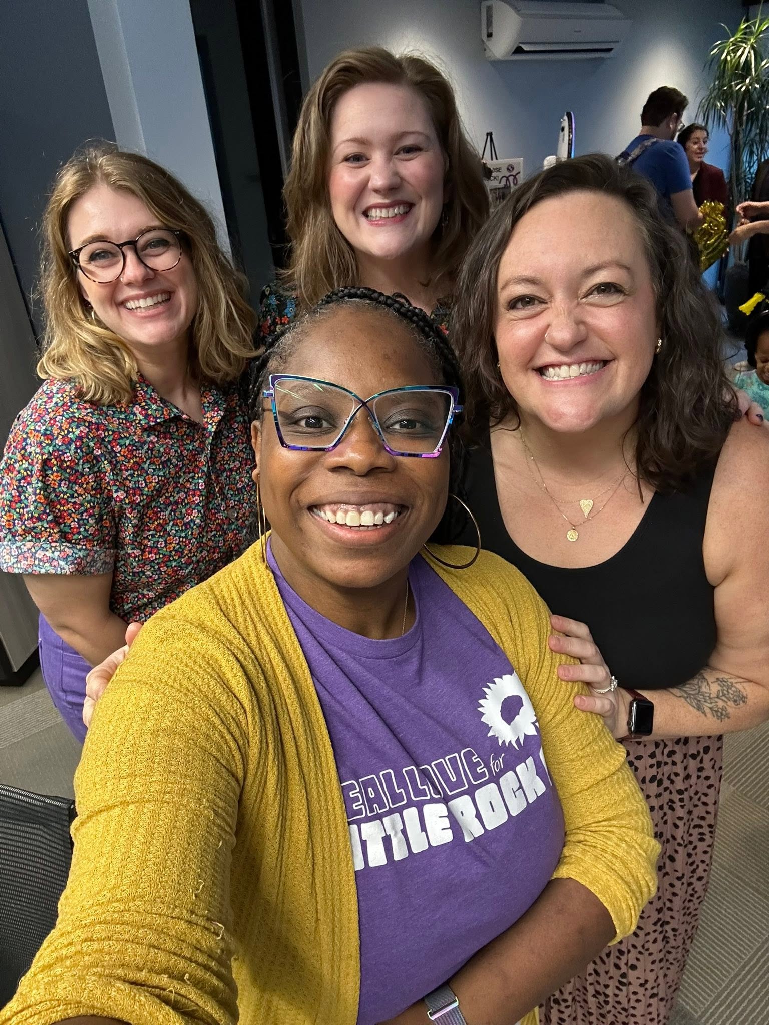 Four friends smiling together, one wearing a Real Love for Little Rock shirt
