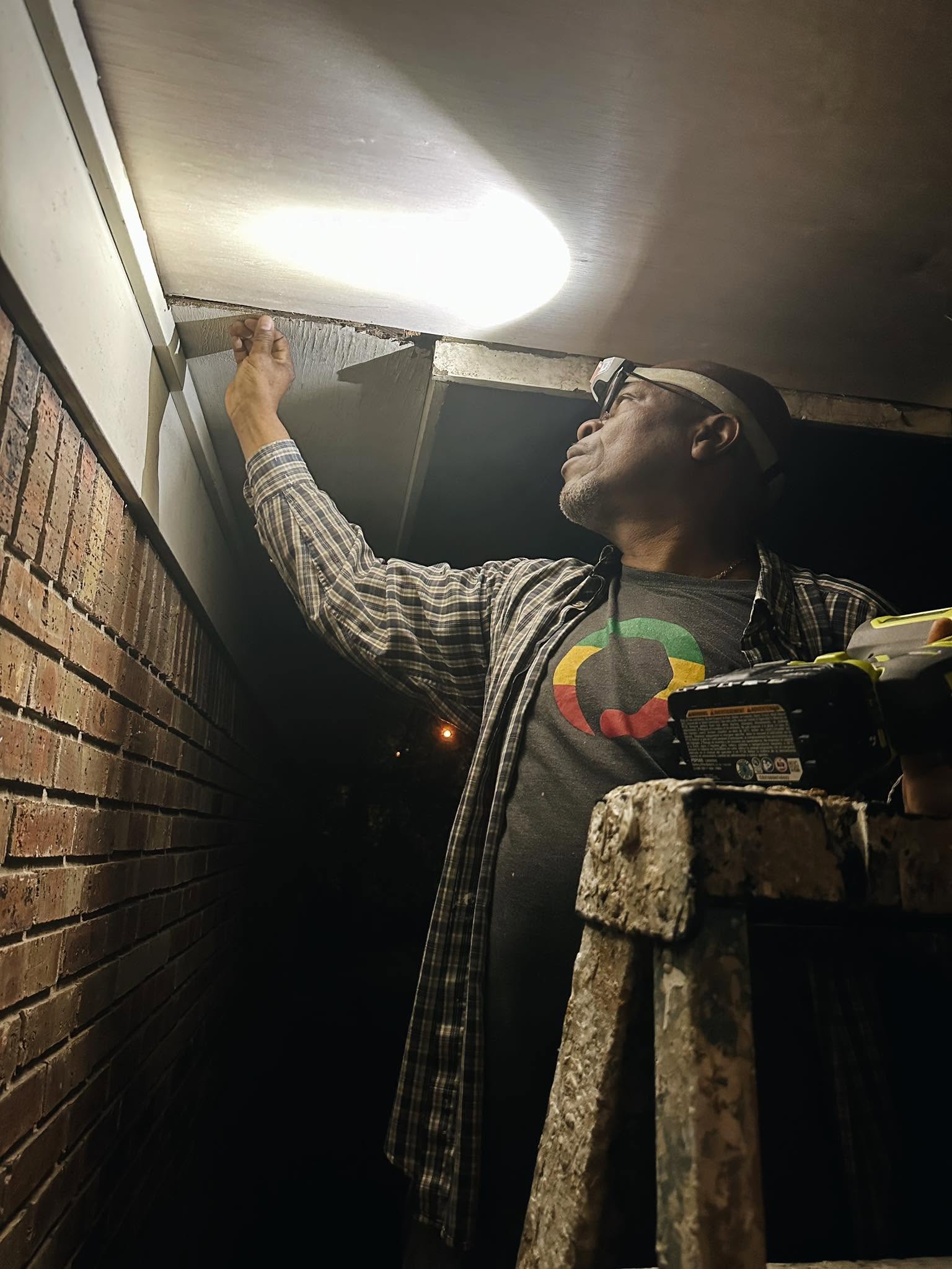A volunteer wearing a headlamp repairs a porch ceiling at night