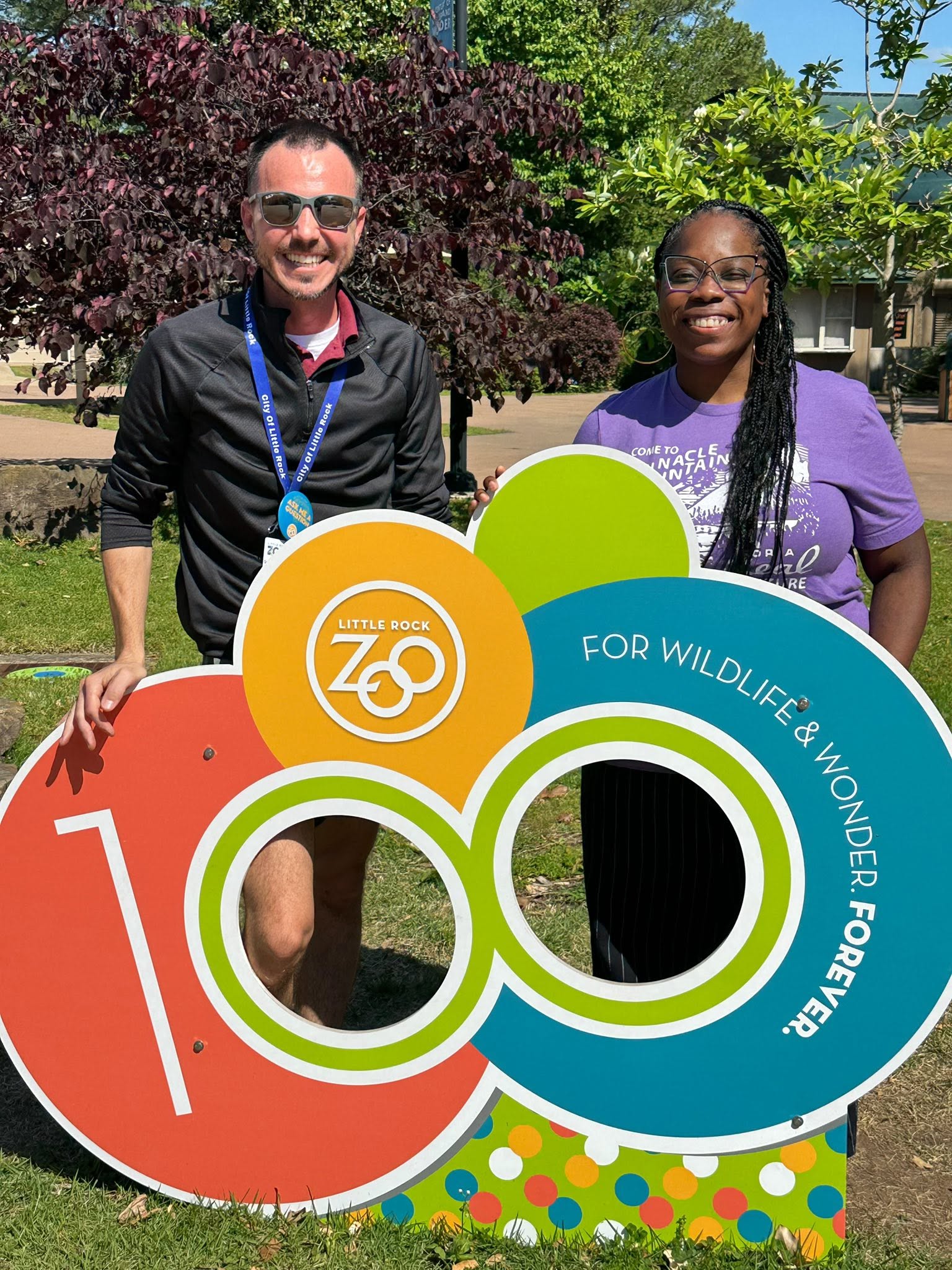 A Little Rock Zoo staff member and a Rocktown Realness organizer smiling behind the zoo’s 100th anniversary sign